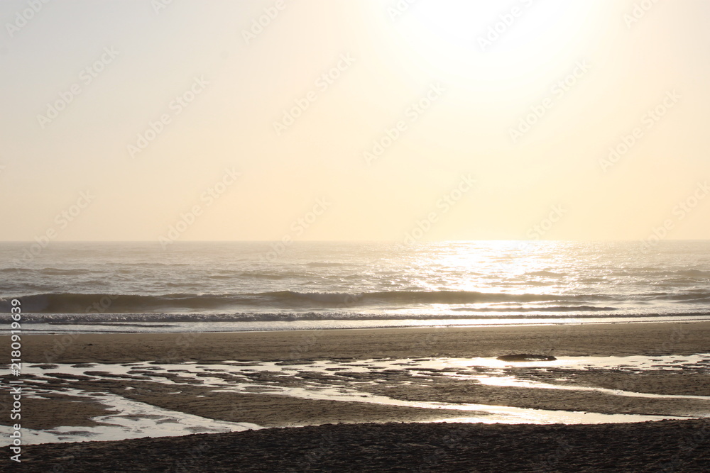 Fototapeta premium Golden Sunset Reflection on Ocean Beach and Wet Sand Tide Pools, Bright Sun Flares Over Calming Waves and Horizon Landscape, Peaceful Coastal Nature Background and Summer Travel Vacation Concept