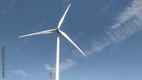 A majestic white wind turbine stands tall against a bright blue sky with wispy clouds, symbolizing clean, renewable energy and a hopeful, sustainable future. There are no people.