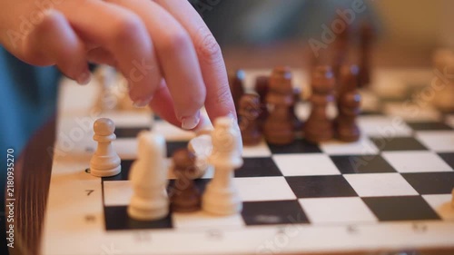 Close up of hand moving chess pieces on checkered board focusing on interaction between white and brown pawns. scene features detailed textures of wooden game components under soft lighting