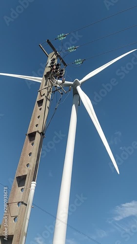 This striking lowangle view shows a concrete utility pole next to a modern white wind turbine against a clear blue sky, evoking hope for a sustainable future. No people.