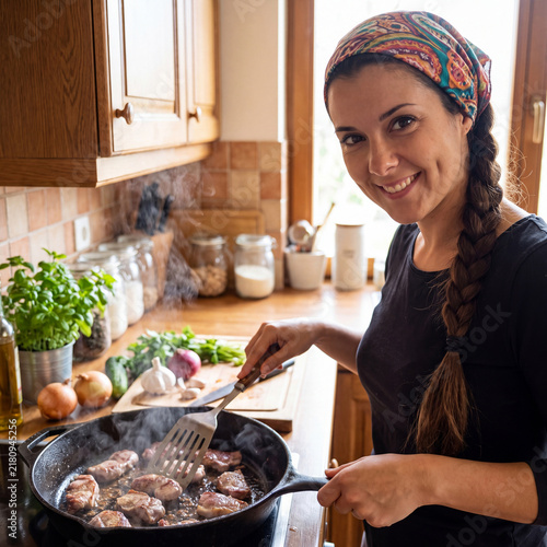 Happy housewife in an apron holds a ready-made dish of baked chicken and potatoes.