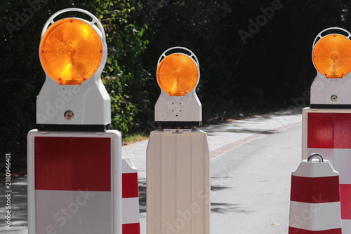 Foto Portable roadwork warning lamps and red white barriers block a narrow street during maintenance
