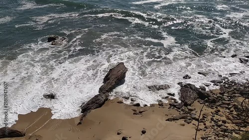 Experience the powerful serenity of nature with this highangle view of ocean waves crashing onto a rugged, rocky sandy beach. It evokes peace and wild solitude. No people.