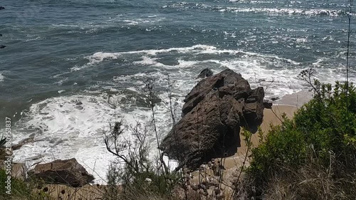 A breathtaking, highangle view of powerful ocean waves crashing against a rugged rock on a secluded sandy shore, evoking raw natural strength and peaceful solitude. Nobody.
