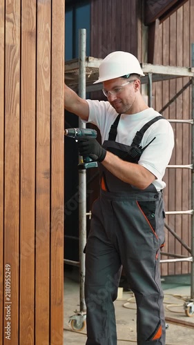 Construction worker using power drill on wooden wall