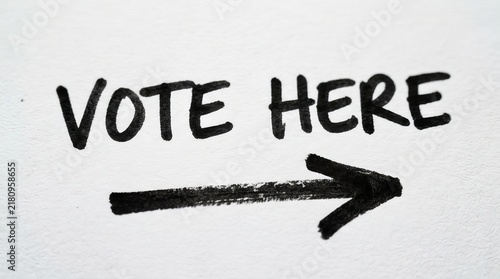 Close Up of Vote Here Sign on Flat White Paper with Bold Black Arrow Indicating Voting Direction