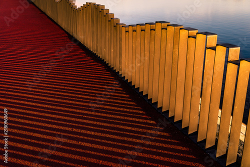 Golden metal balustrade casting long shadows on red path at sunset.