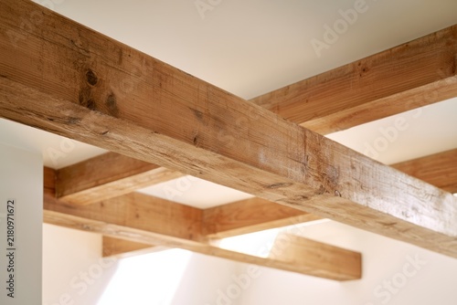 Rustic wooden ceiling beams crossing each other in a bright modern interior space with natural light filling the room