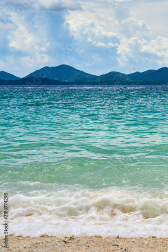 Принти на полотні Tropical Turquoise Sea with Gentle Surf and Island Mountains Under Cloudy Sky