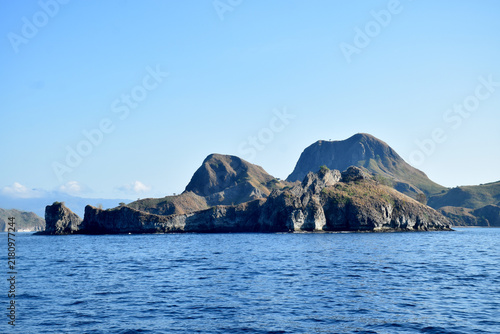 Sailing to Komodo Island in clear weather, passing rugged hills amidst the crystal-clear waters of Rinca Island, Labuan Bajo, Indonesia.