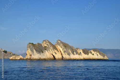 Sailing to Komodo Island in clear weather, passing rugged hills amidst the crystal-clear waters of Rinca Island, Labuan Bajo, Indonesia.