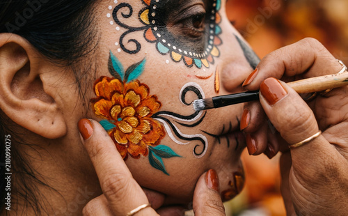 Woman getting traditional Day of the Dead face paint applied for cultural celebration festival portrait