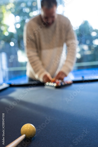Adult man in sweater leaning on blue-felt pool table racking at home with cue ball, cue-stick