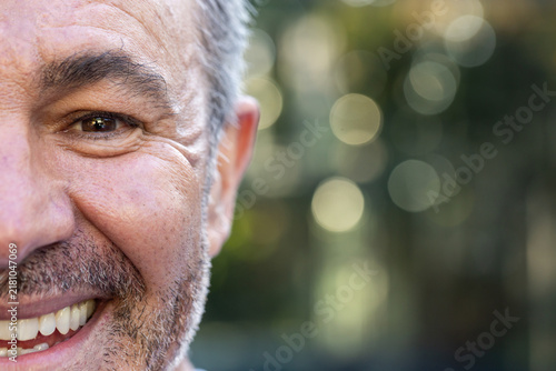 Middle-aged man smiling and facing camera in garden with bokeh foliage background, copy space