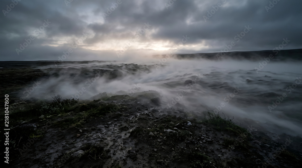 Fototapeta premium Fog rolling over a rocky coastal landscape under a dramatic cloudy sky