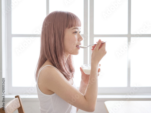 Obraz w ramie 大きな窓から朝日が差し込む部屋で朝食をとる女性