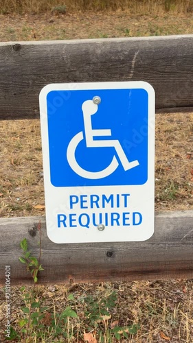 Vertical format of a blue and white sign showing a figure in a wheel chair with the words Permit Required underneath, most likely for an outdoor parking spot reserved for people with disabilities. 