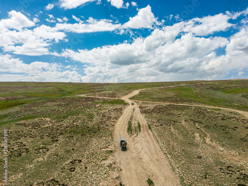 Fotografie An agricultural tractor driving across the remote, rolling green alpine steppe o