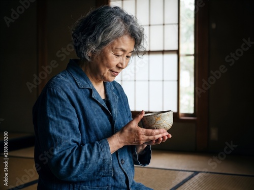Portrait of a thoughtful senior Asian woman admiring a traditional kintsugi ceramic bowl in a serene Japanese room with shoji screens, wabi sabi philosophy and appreciation of imperfect beauty