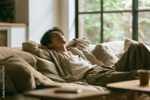 Obraz na płótnie 眼鏡をかけリネンのソファでリラックスし目を閉じる日本人男性、デジタルデトックス