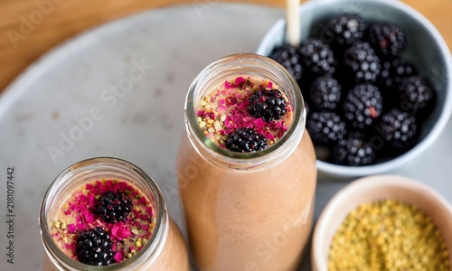 Top view of healthy berry smoothie in glass bottles garnished with fresh blackberries, bee pollen, and dried flower petals