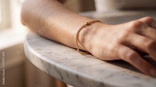 Close-up of a delicate gold bracelet on a woman wrist resting on a marble table