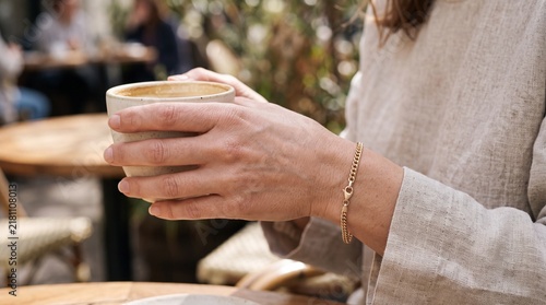 Close-up of a Person Holding a Warm Ceramic Coffee Cup in an Outdoor Cafe Setting