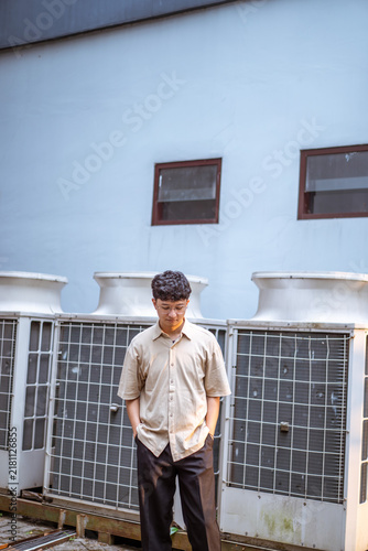 Fotografie A young man stands in front of a blue wall with large white structures, looking down