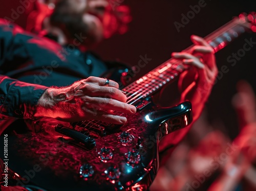 Close-up of a musician playing an electric guitar with red stage lighting