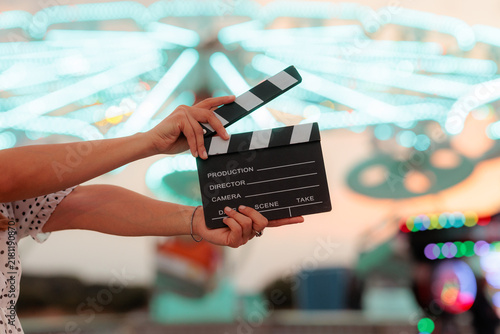 Hands Holding Movie Clapperboard At Colorful Amusement Park Neon Fairground. Person holding a black cinema clapper board against bright  carnival lights