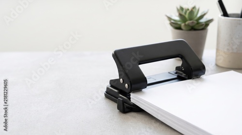 Close Up of Black Paper Punch on Grey Desk with Blank Paper