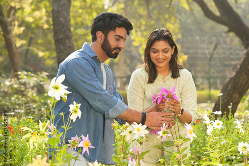 Foto Beautiful indian young couple admiring and holding pink flowers together in a lush green park, enjoying a romantic outdoor moment surrounded by nature