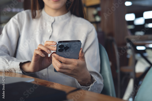 Asian business woman using smartphone with laptop computer and notebook on table, online working at modern office, closeup. Woman using mobile phone for social media network.