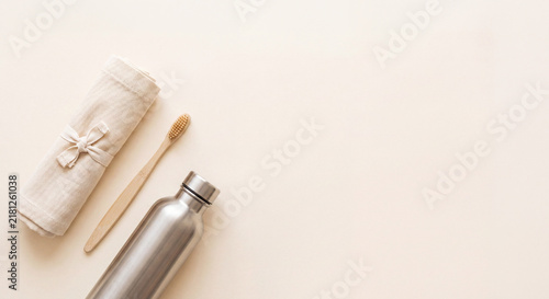 Eco friendly sustainable lifestyle flat lay with reusable stainless steel water bottle, bamboo toothbrush, and cotton towel on beige background.