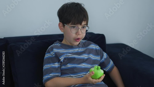 cute young boy with glasses eating a fresh green apple. Healthy childhood nutrition, daily vitamin snack, and casual indoor lifestyle portrait of a kid enjoying organic fruit.