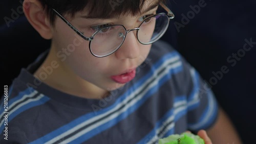 cute young boy with glasses eating a fresh green apple. Healthy childhood nutrition, daily vitamin snack, and casual indoor lifestyle portrait of a kid enjoying organic fruit.