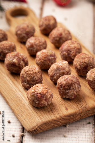 Uncooked minced beef meat balls for cooking on rustic wood board with herbs and tomatoes on white table