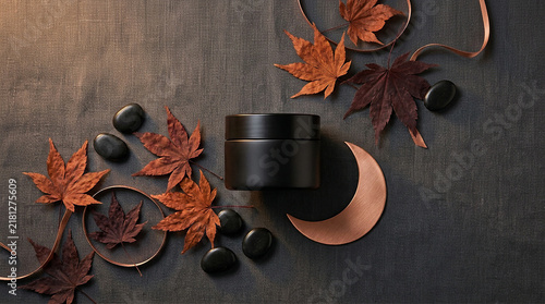 Top view of matte black skincare jar with autumn maple leaves and black stones cosmetic packaging fall theme beauty product skincare branding minimalist des