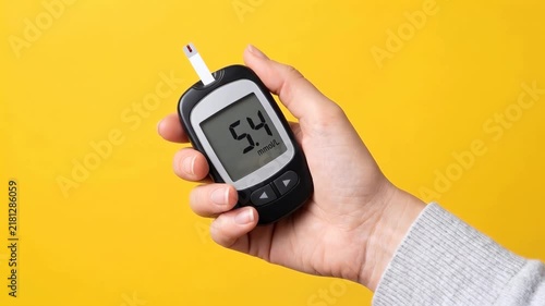 POV close-up of a female hand holding a digital blood glucose meter with healthy blood sugar reading on screen. Diabetes control, wellness and healthcare monitoring concept