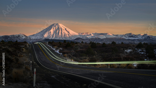 Long exposure image of car light trail on Desert Road at dawn. Snow-capped Mt Ngauruhoe in the distance. North Island. New Zealand.