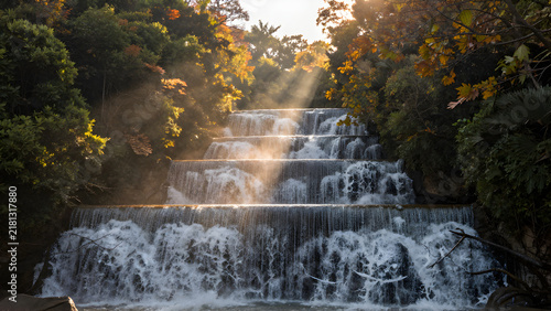 Sunlit multi-tiered waterfall cascading through autumn forest