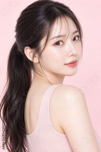 Fototapeta ピンク背景で肩越しに振り向く日本人女性の透明感ある美容スキンケアポートレート