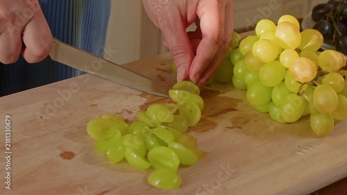 Person cuts fresh green grapes with knife on wooden board in bright kitchen setting, demonstrating food preparation technique with close up camera work.