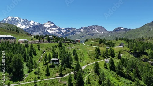 Aerial view of the scenic Simplon Pass in the Swiss Alps during summer, featuring winding mountain roads, green alpine slopes and dramatic peaks under a clear blue sky.