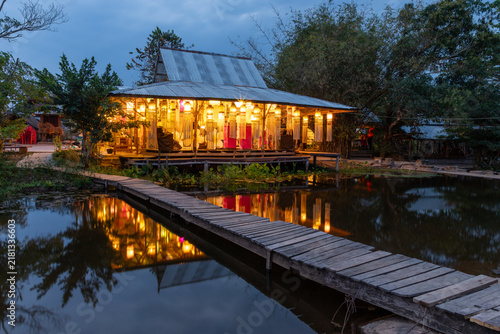 Illuminated traditional wooden pavilion and wooden footbridge reflecting on a pond at twilight.