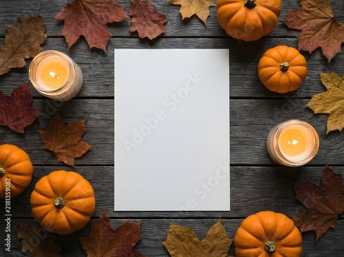 Blank white paper mockup surrounded by autumn pumpkins and glowing candles on a rustic wooden background