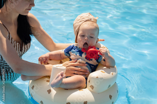 Obraz na plátně Mother watches her baby play with a crab toy in a swimming pool float