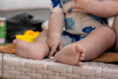 Close up of a baby's feet and legs sitting on a wicker chair outdoors