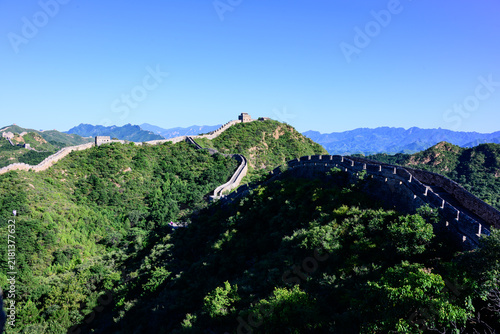 Quadro su tela The Jinshanling Great Wall, an ancient stone fortification, winds across lush green mountain slopes under a vivid blue sky, with steep stone steps and aged watchtowers rising amid dense vegetation