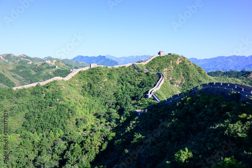 Canvastavla The Jinshanling Great Wall, an ancient stone fortification, winds across lush green mountain slopes under a vivid blue sky, with steep stone steps and aged watchtowers rising amid dense vegetation